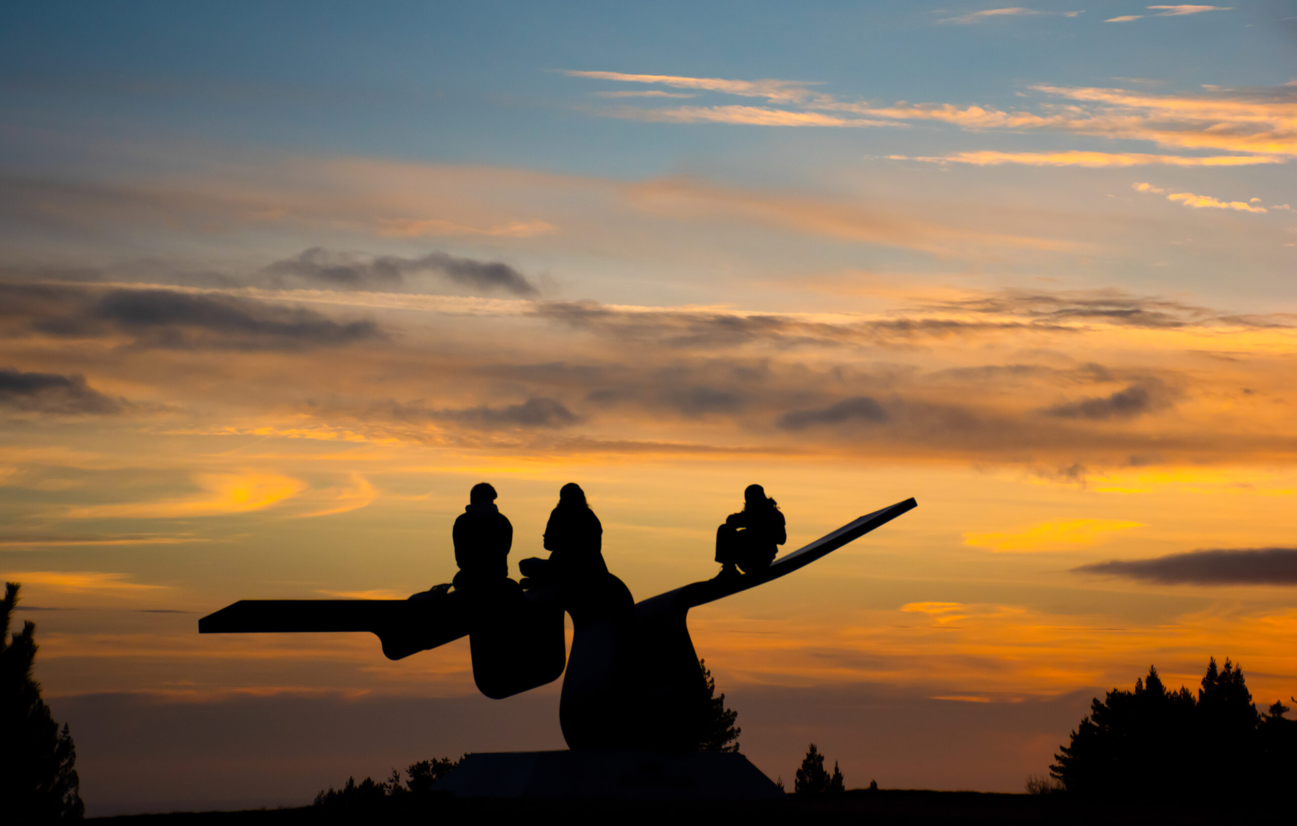 Three students sit on the "porter squiggle" sculpture to watch the sunset