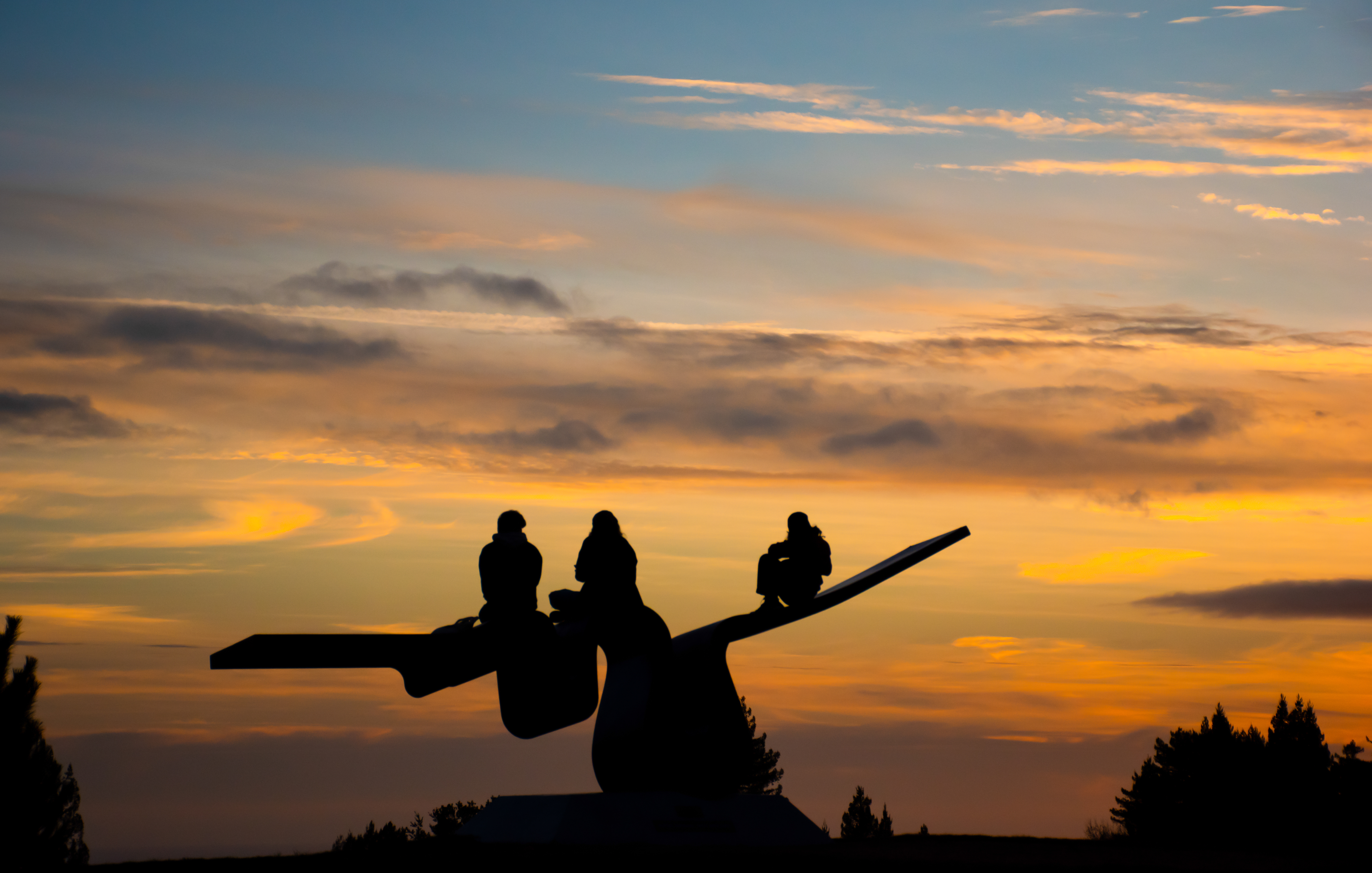 Three students sit on the "porter squiggle" sculpture to watch the sunset