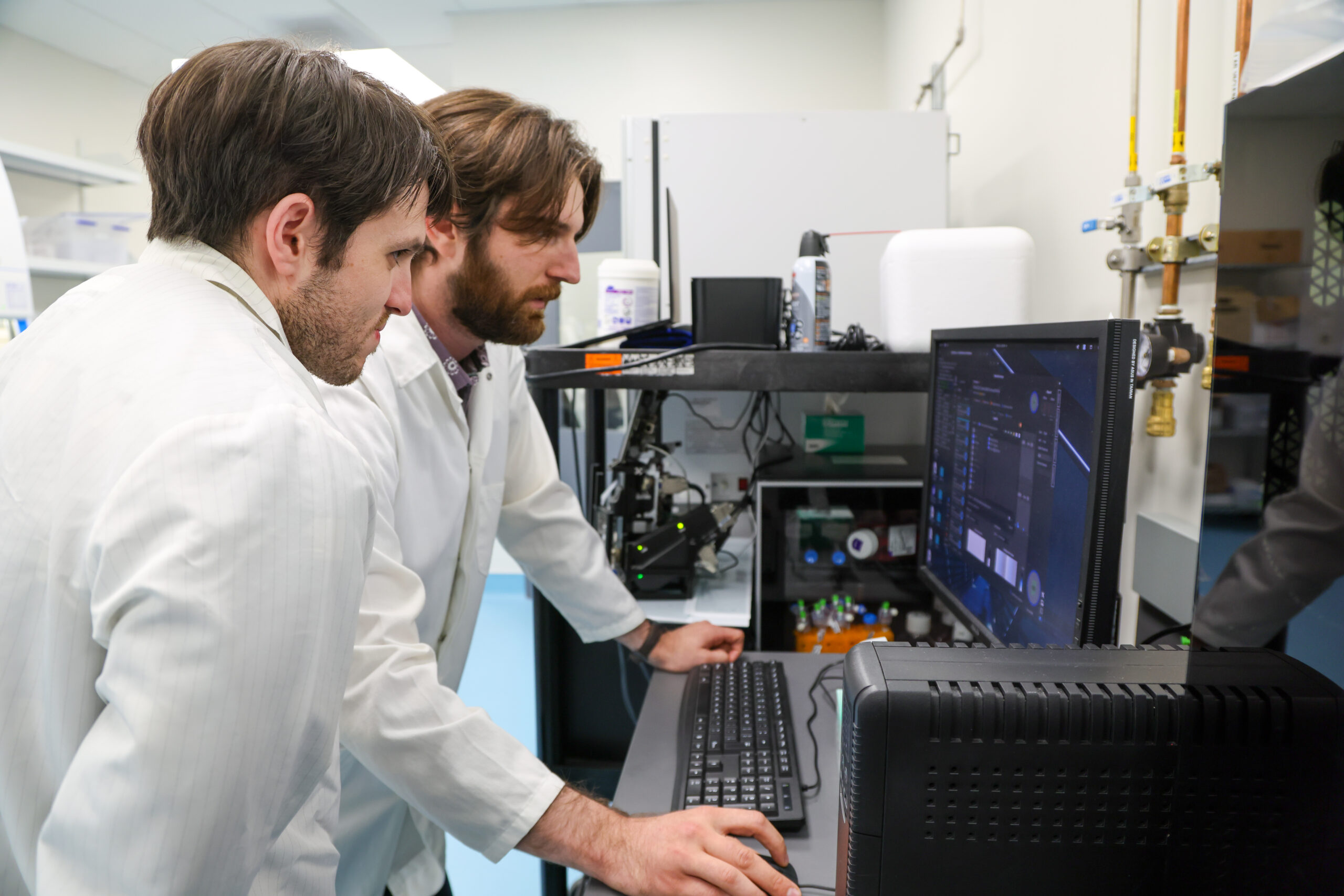 Two men in lab coats at a computer screen.