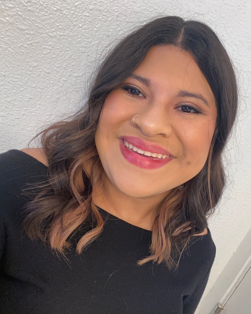 A smiling woman with long brown wavy hair wearing black dress