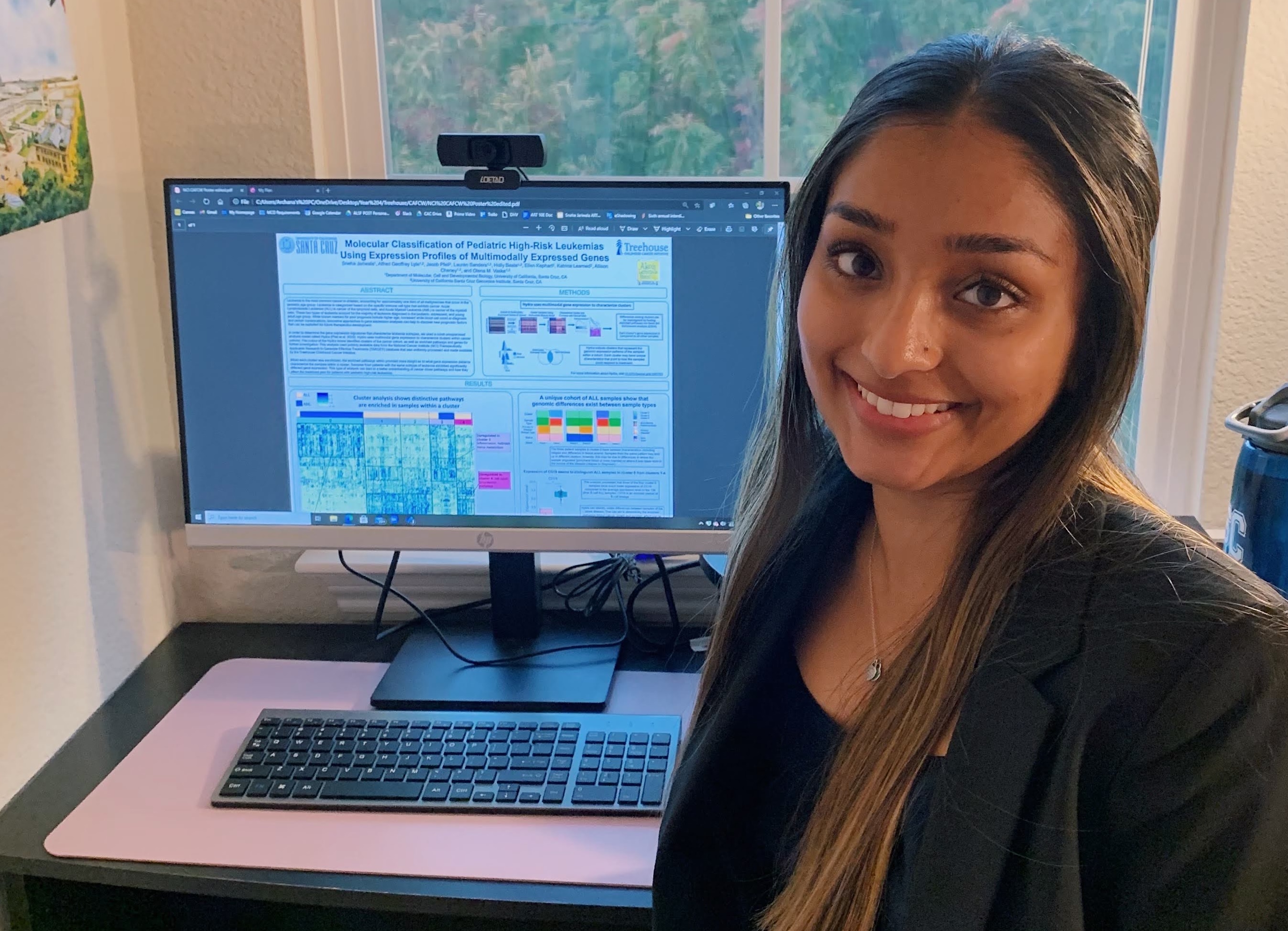 A young woman stands in front of a computer displaying a scientific poster.