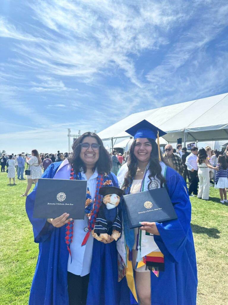 Isha and Andrea wearing their cap and gowns, holding up their degrees at graduation