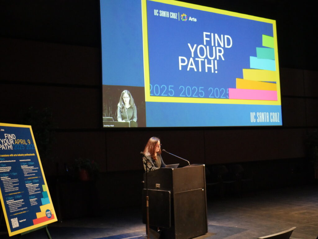 A woman speaking at a podium in a lecture hall with a Find Your Path slide on the screen behind her. 