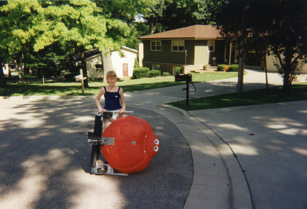 A young Lisa Winter poses for a photo with her robot creation in a driveway. 