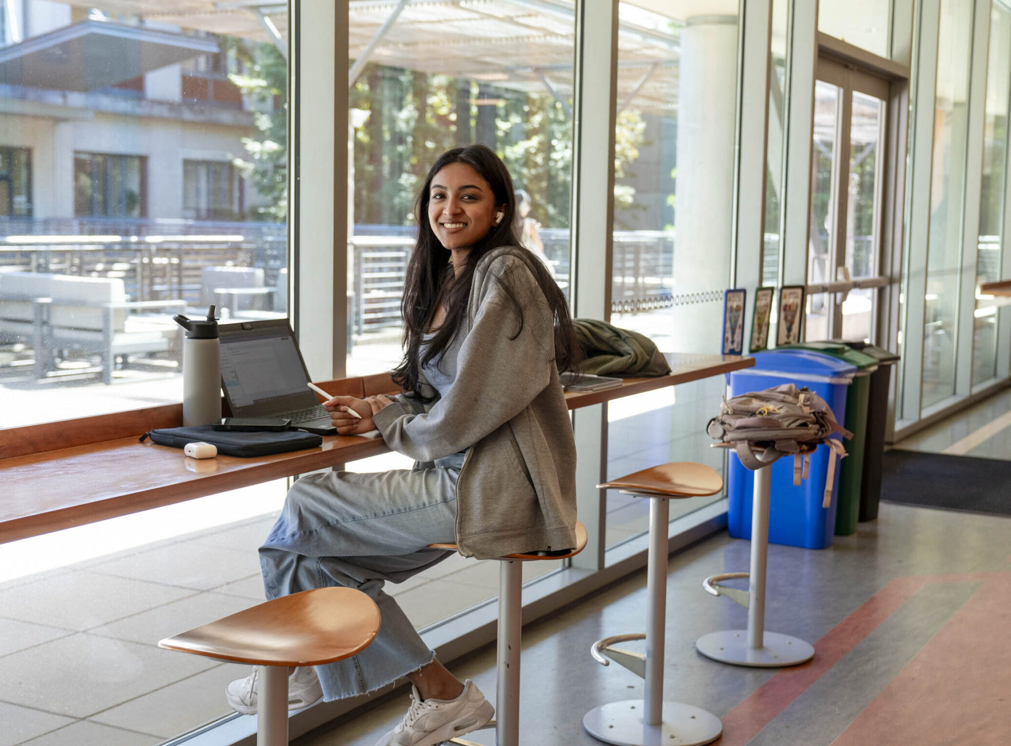 Student smiles while sitting at a long table with a laptop in front of her.