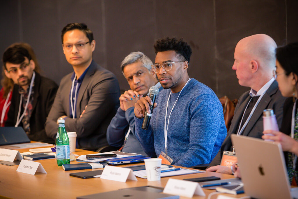 A man speaks into a mic while others look on.
