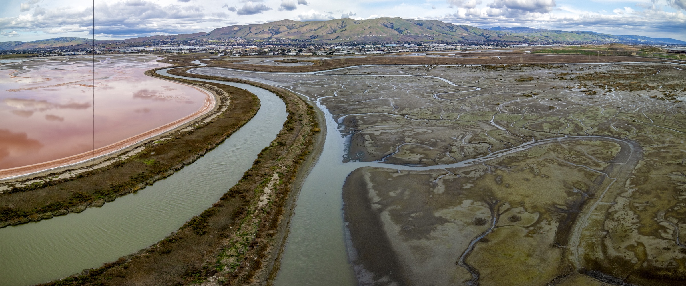 Aerial photo of reddish pond at left and a pond on the right full of plants.