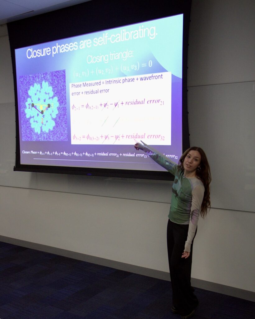 Postdoctoral researcher pointing to presentation projected on a screen in front of a classroom