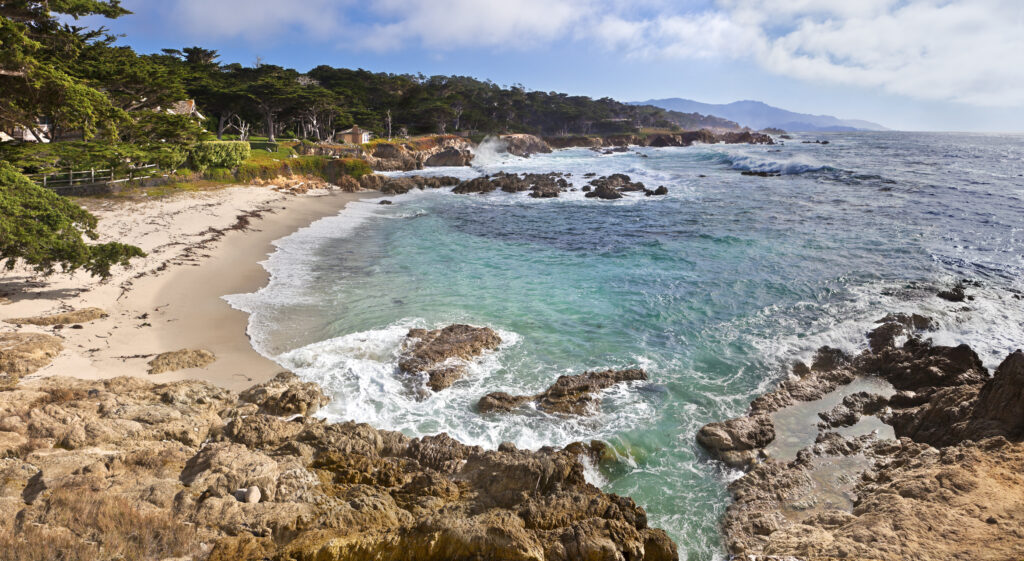 Playa apartada de aguas azules y cristalinas, con olas rompiendo cerca de grandes casas.