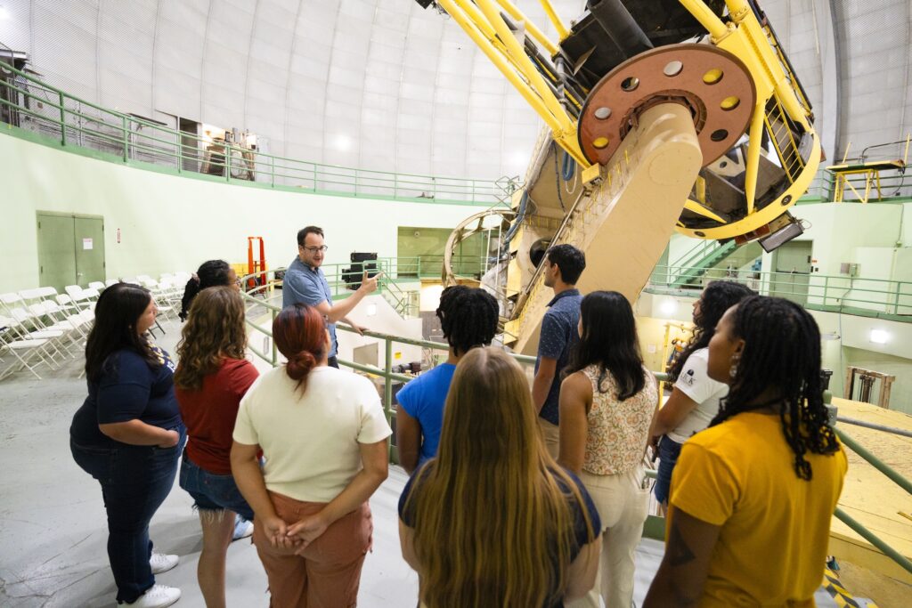 Class standing on a platform next to large telescope