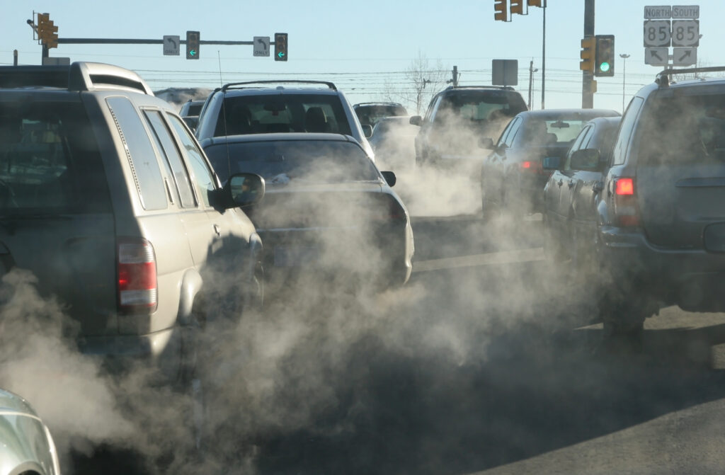 Clouds of car exhaust amidst a line of cars on a roadway