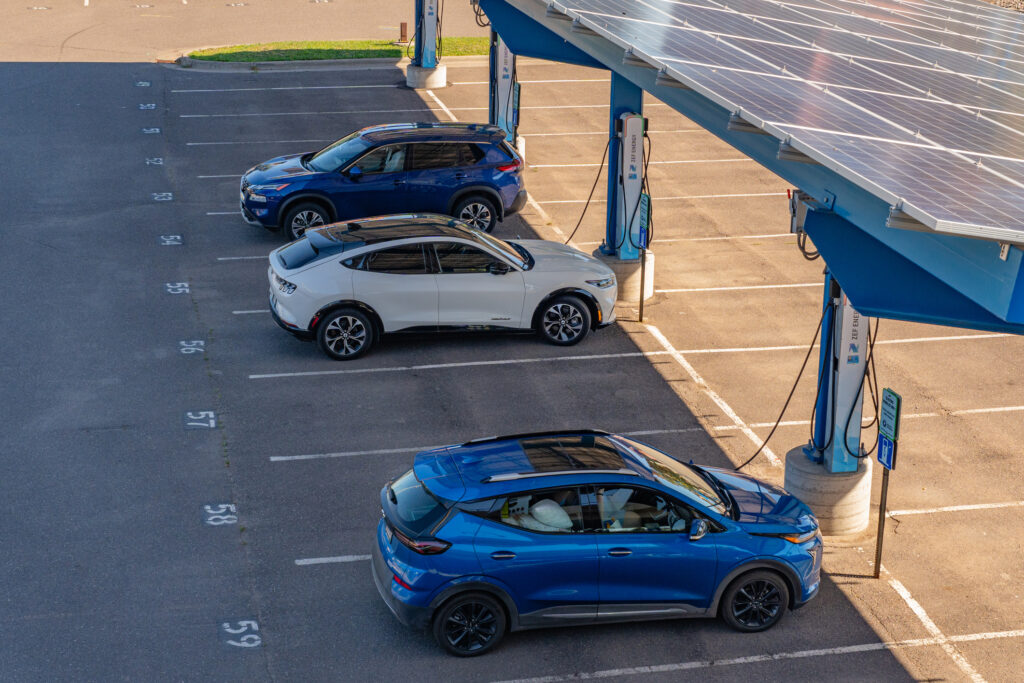 Three cars plugged into charging infrastructure shaded by solar panels