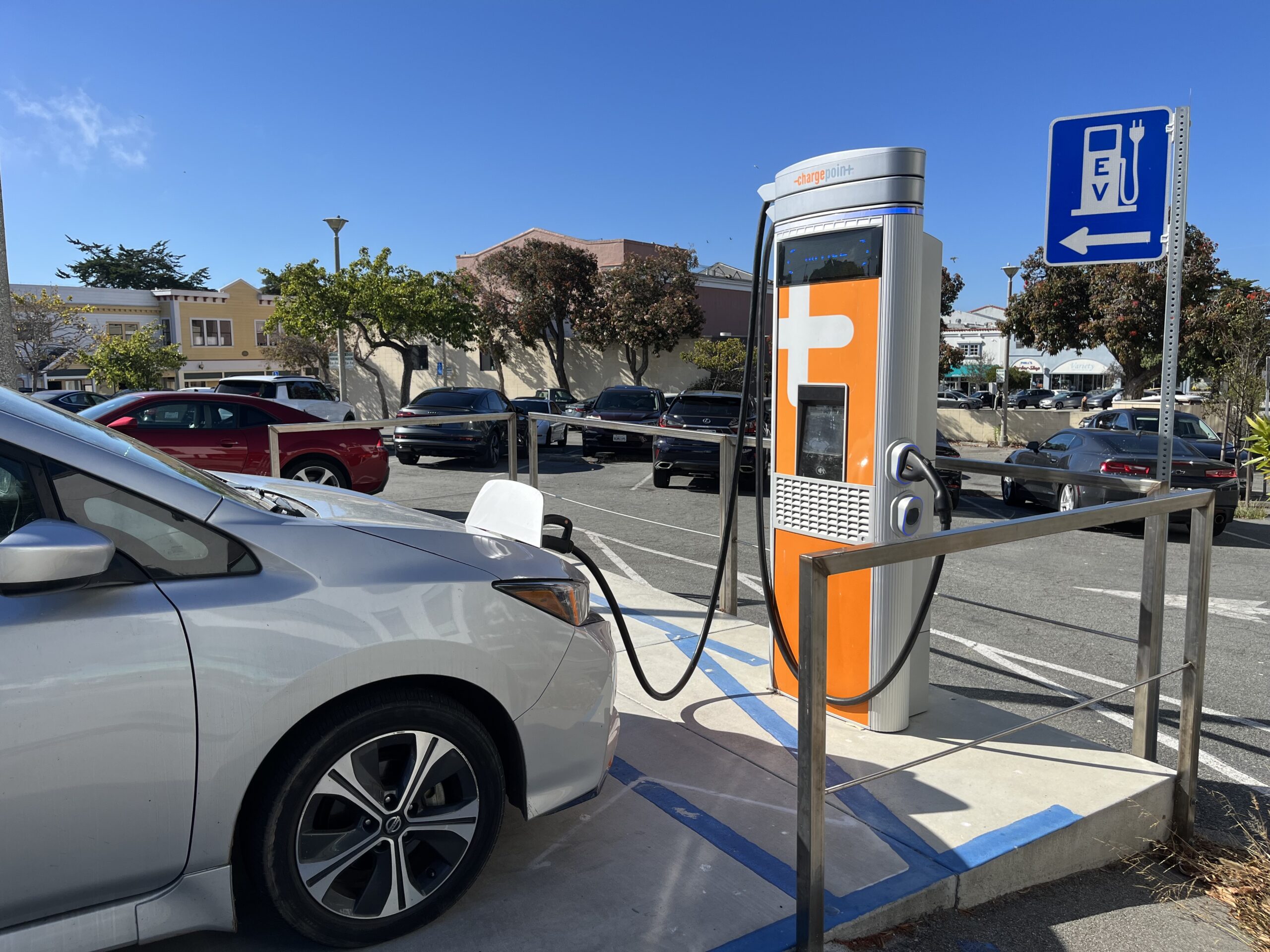 Car plugged in to a charger in a parking lot of a downtown area, with an "EV" sign.