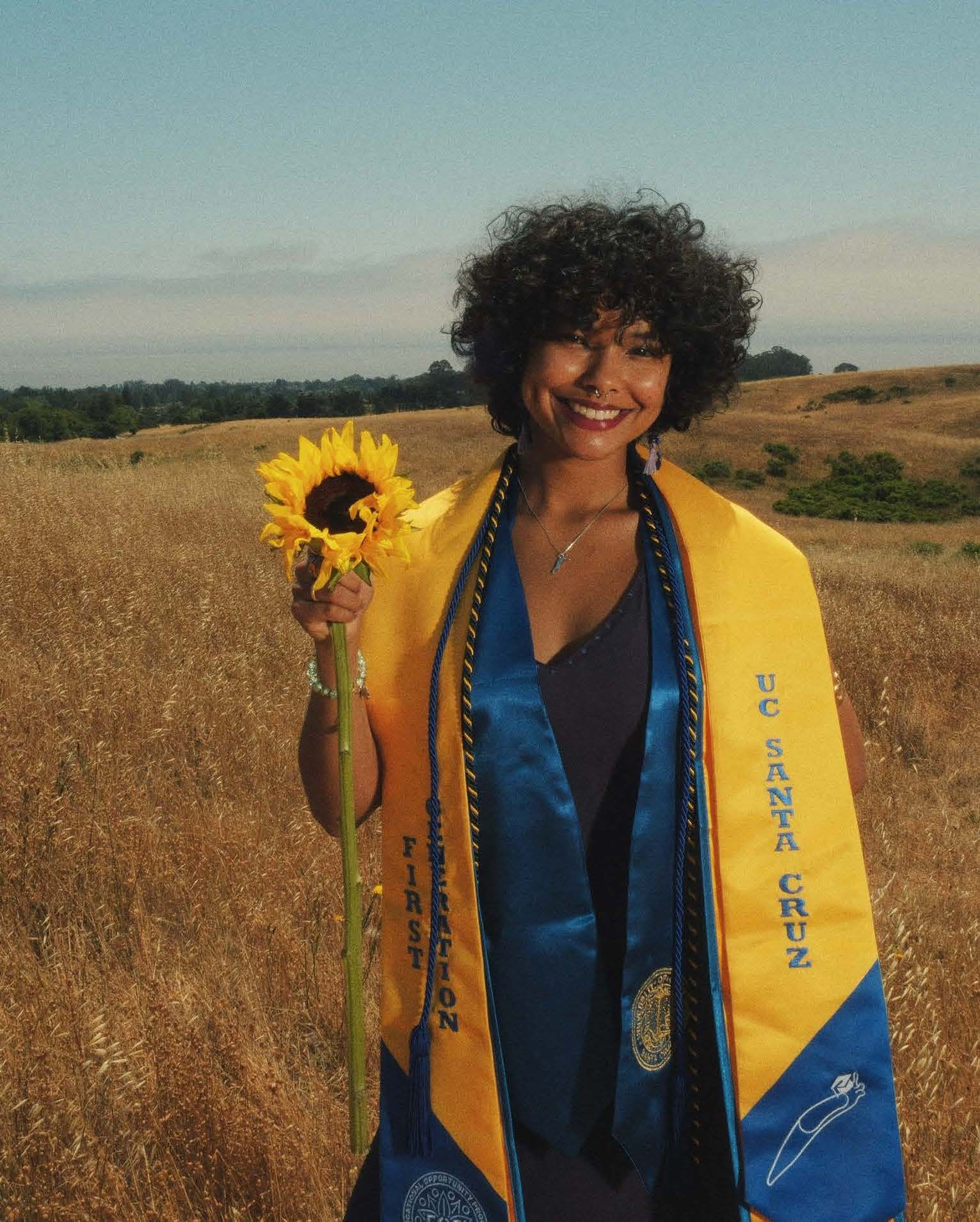Maddison Brodeur poses with a sunflower at a UC Santa Cruz meadow in graduation gear.