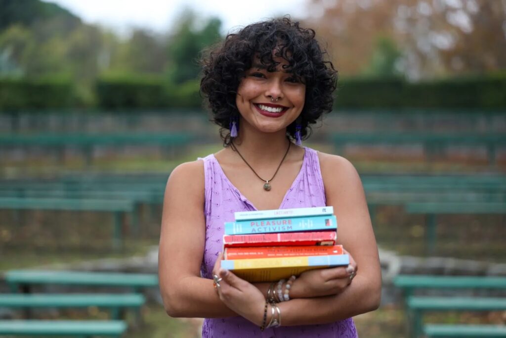 Maddison poses for a photo with a stack of books in hand.