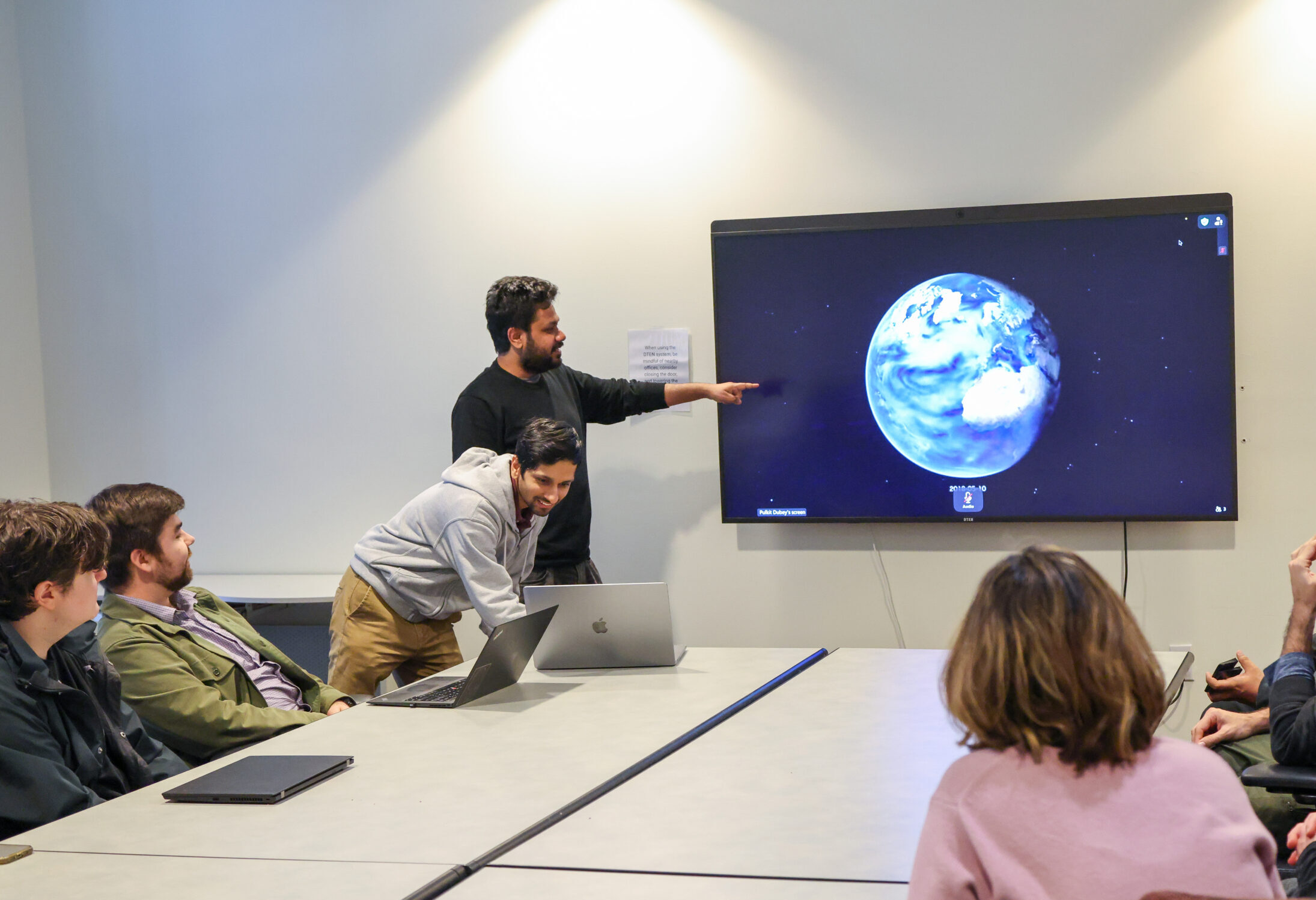 Man points at a screen displaying an image of the Earth in a classroom
