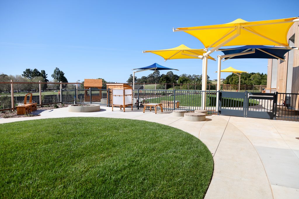 Early Education Center play yards with yellow sun shades and green grass.