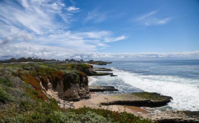Southward-facing photo of Santa Cruz's West Cliff stretching into the distance on a partly cloudy day.