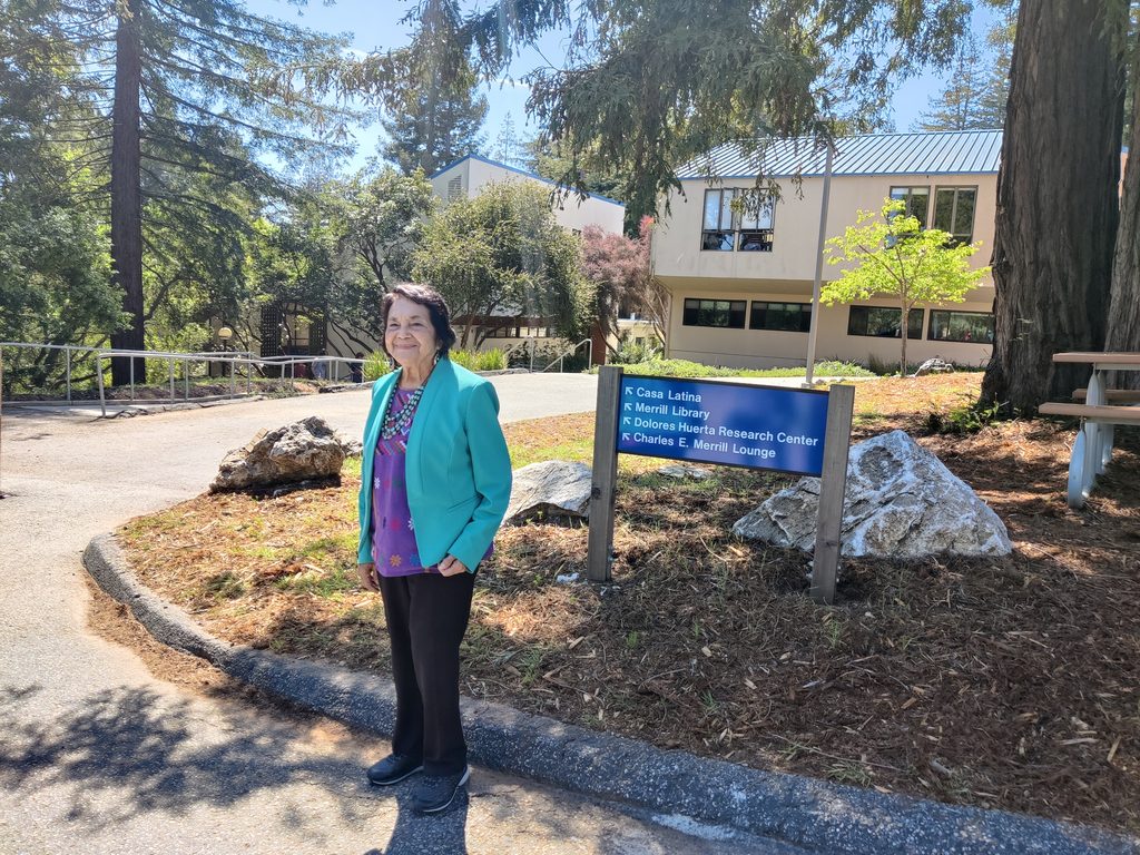 Dolores Huerta smiles in front of a sign for the Huerta Center on campus.