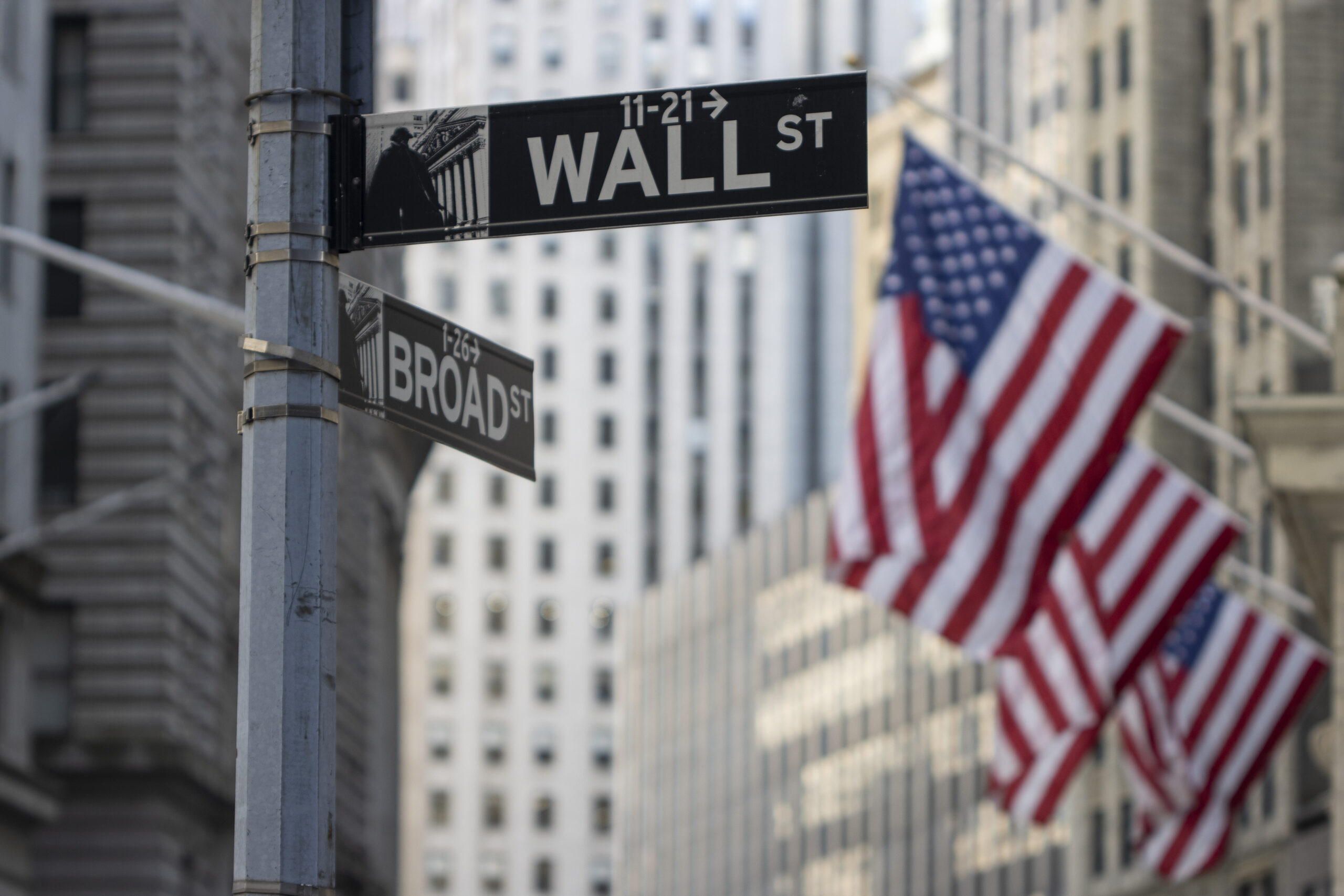 A sign post showing wall street and broad street, with American flags.
