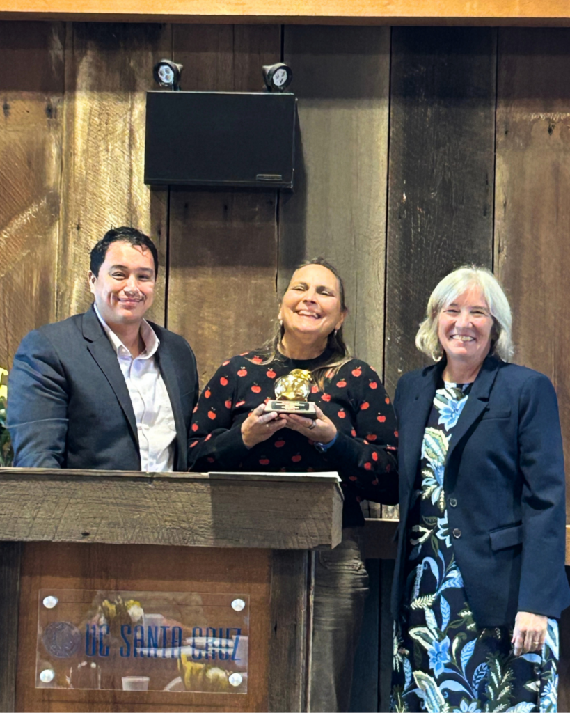 three people dressed up with center person holding golden apple award