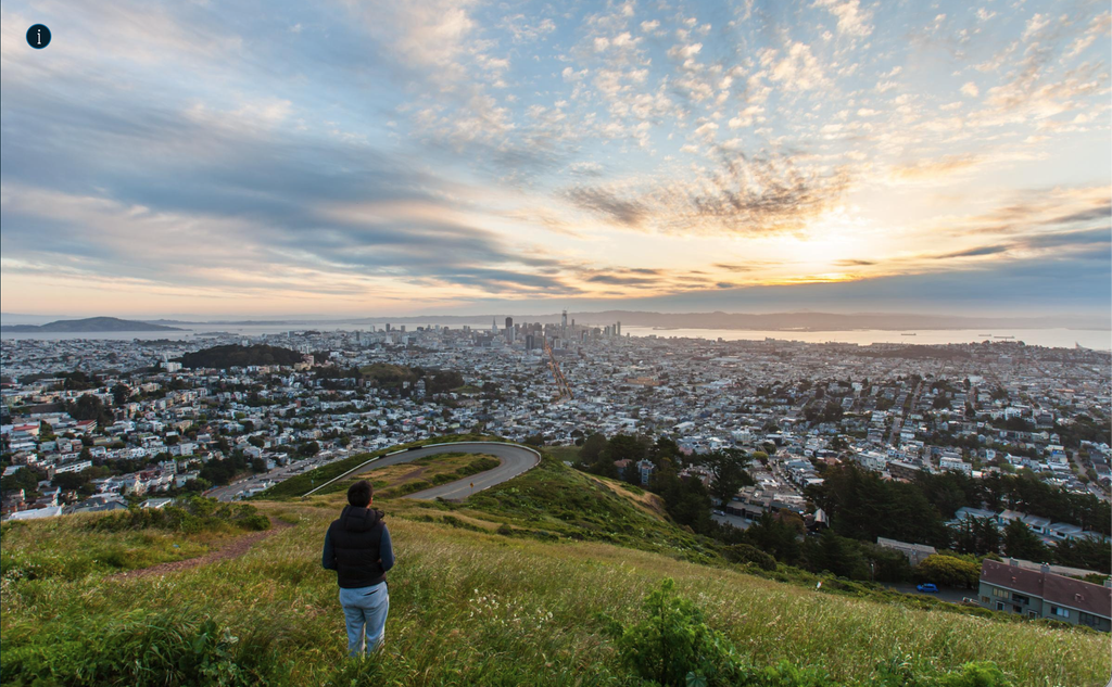 Person on a grassy hill overlooking San Francisco at sunset