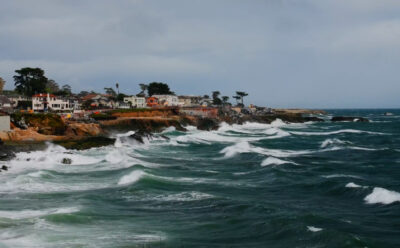 Large waves hit a shoreline against a cloudy sky