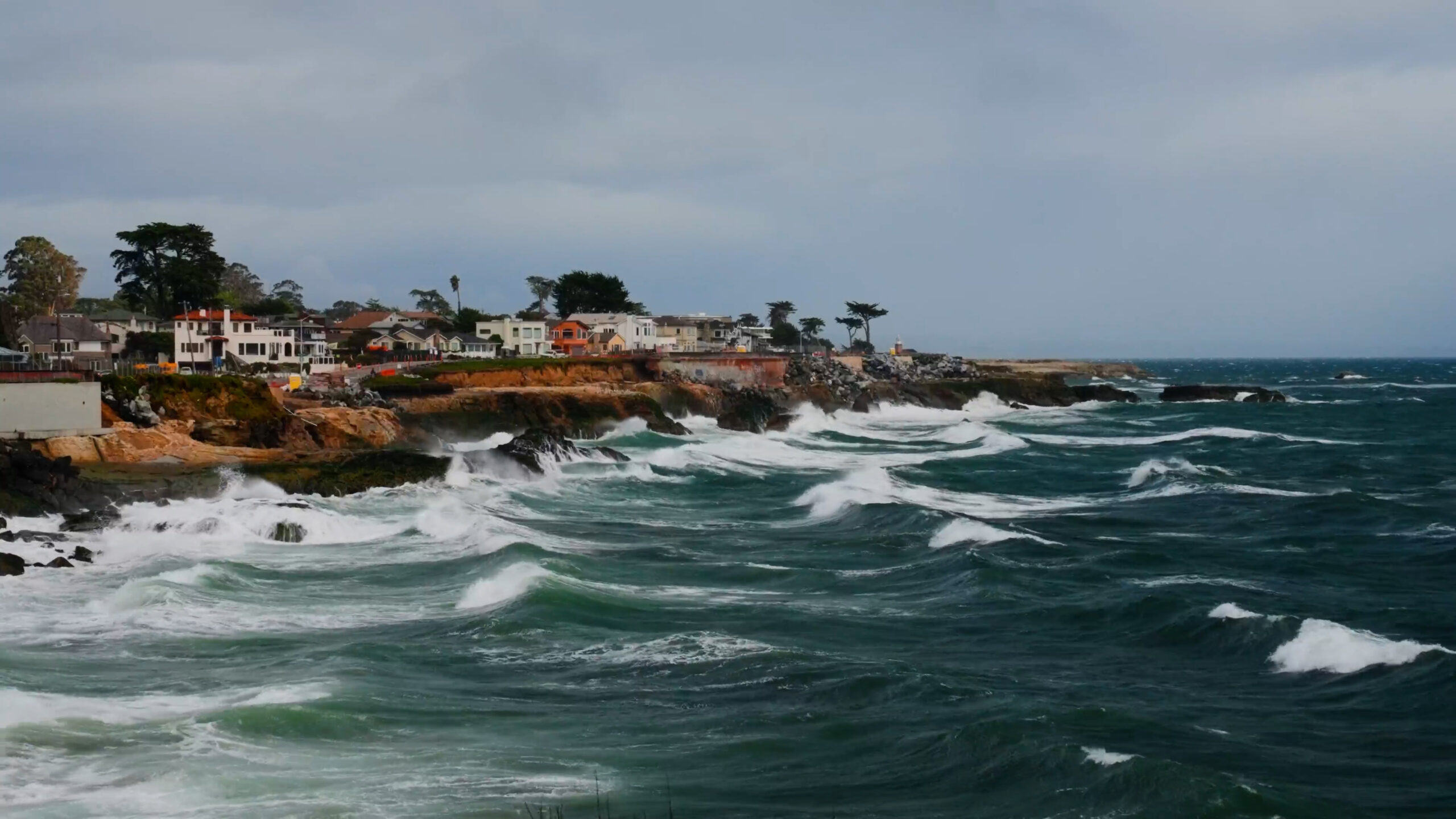 Large waves hit a shoreline against a cloudy sky